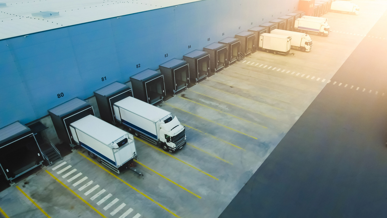 Aerial Shot of Industrial Warehouse Loading Dock where Many Truck with Semi Trailers Load Merchandise.